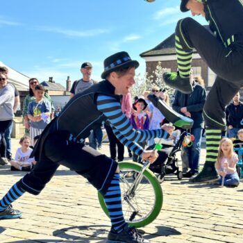 One unicyclist holding a uni cycle and another jumping on feet first