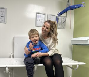 Photo of Charlie, sat on the bench in the Changing Places toilet next to his mum.
